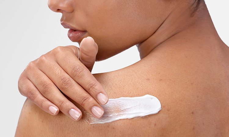 Eine Frau trägt Creme auf die Haut im Bereich ihres Schulterblatts auf