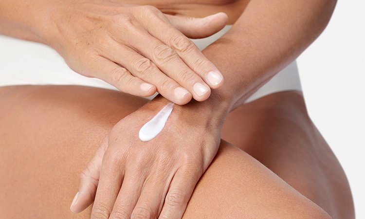 Eine Frau trägt eine Bodylotion auf Beine und Arme auf