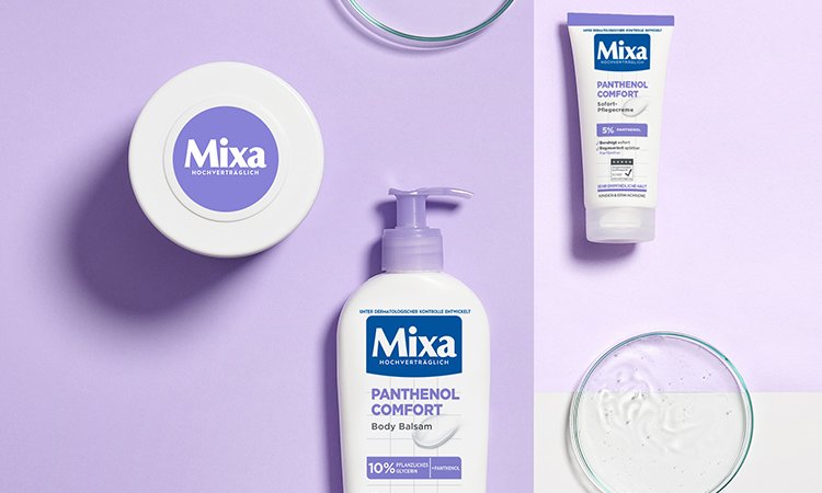 Die Hautberuhigende Creme, der Body Balsam und die Sofort Pflegecreme der Panthenol Comfort-Reihe von Mixa liegen auf einer lilafarbenen Fläche.