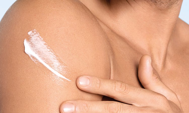 Ein Mann cremt sich mit der linken Hand den rechten Oberarm mit einer Creme mit Sheabutter ein