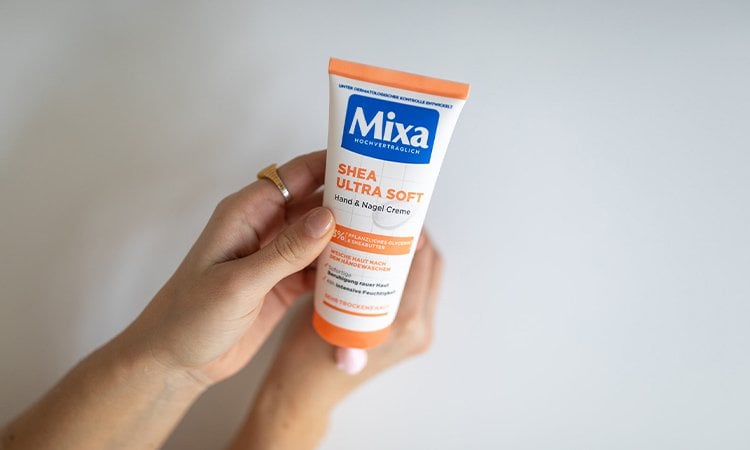 Zwei Hände einer Person mit einem Ring am linken Zeigefinger halten eine Handcreme, während sie die Creme auf die rechte Hand aufträgt. Zwei Hände einer Person mit einem Ring am linken Zeigefinger halten eine Handcreme, während sie die Creme auf die rechte Hand aufträgt.