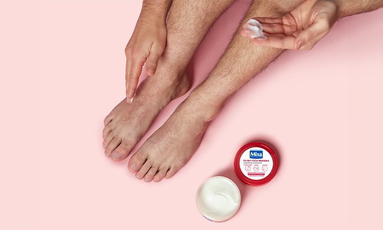 Eine Person cremt ihre trockenen Füße mit der MIXA Cica Repair Creme ein.
