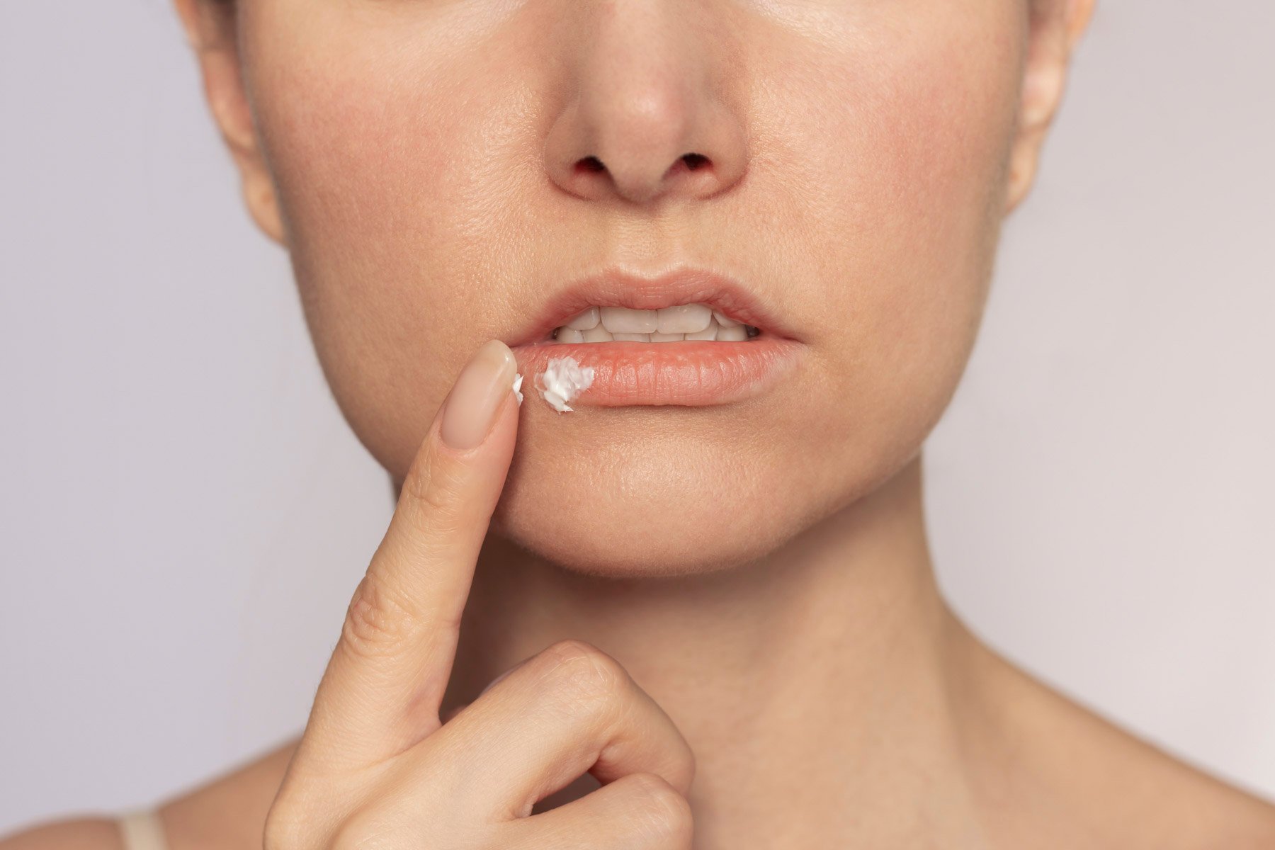 Person trägt Lippenbalsam/Creme auf die Unterlippe auf.