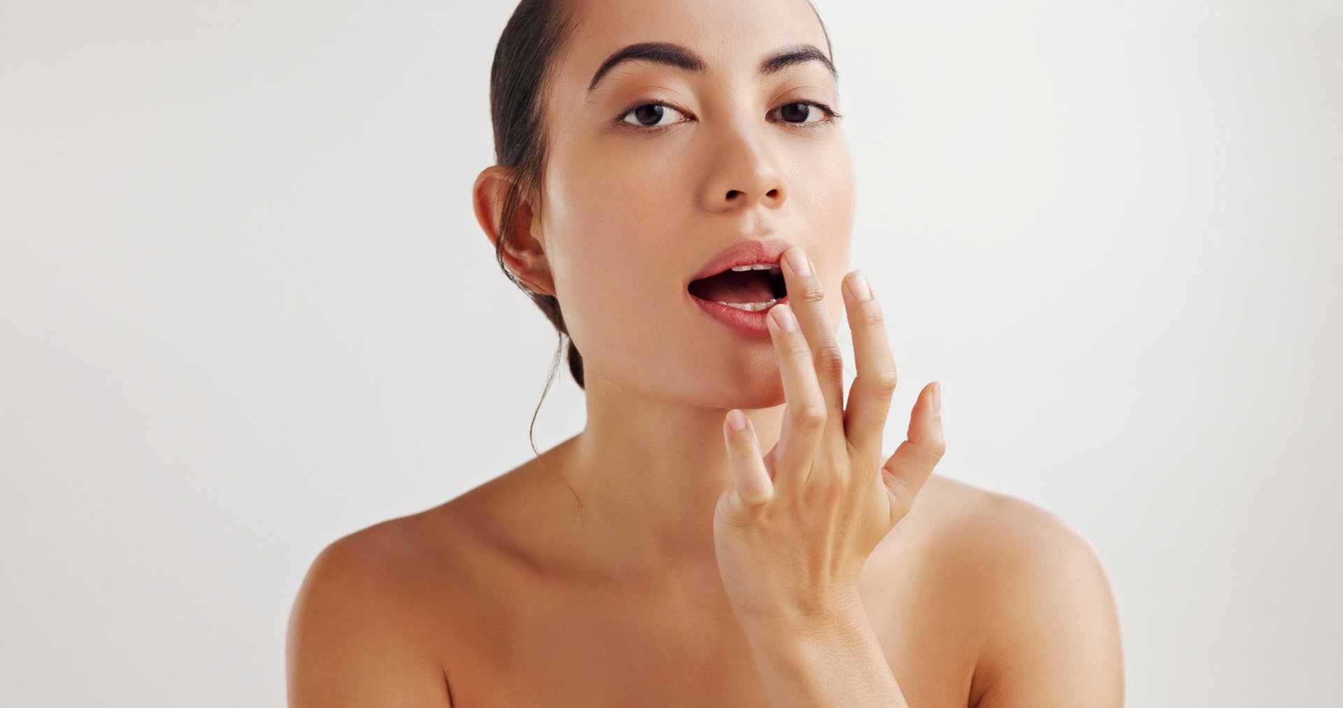 Frau trägt mit dem Finger Lippenpflege auf und hat den Mund leicht geöffnet.