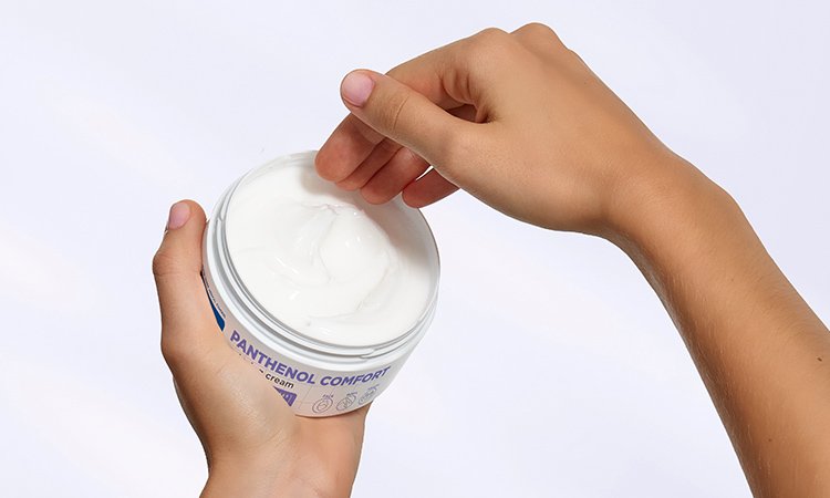 Aus einem offenen Tiegel, von einer Hand gehalten, wird Creme entnommen