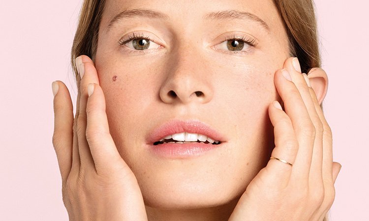Eine Frau trägt ein Serum auf die Wangenpartie im Gesicht auf