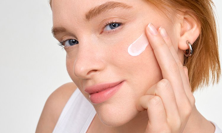 Eine Frau trägt mit zwei Fingern eine Feuchtigkeitscreme auf ihren Wangen auf