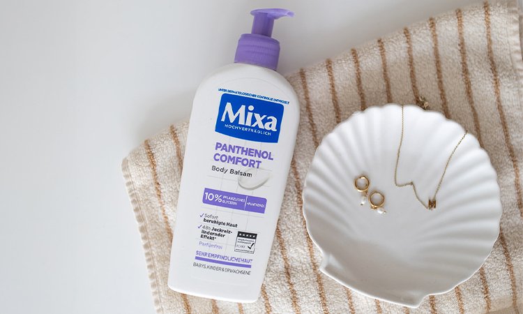 MIXA Panthenol Comfort Body Balsam - Produkt auf einem Handtuch liegend neben einer kleinen weißen Schale