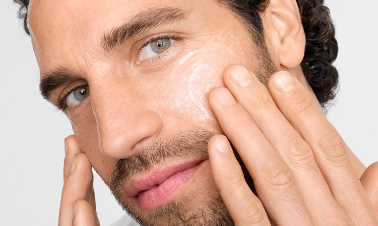 Ein Mann trägt mit zwei Fingern Creme auf der Wangenpartie im Gesicht auf.