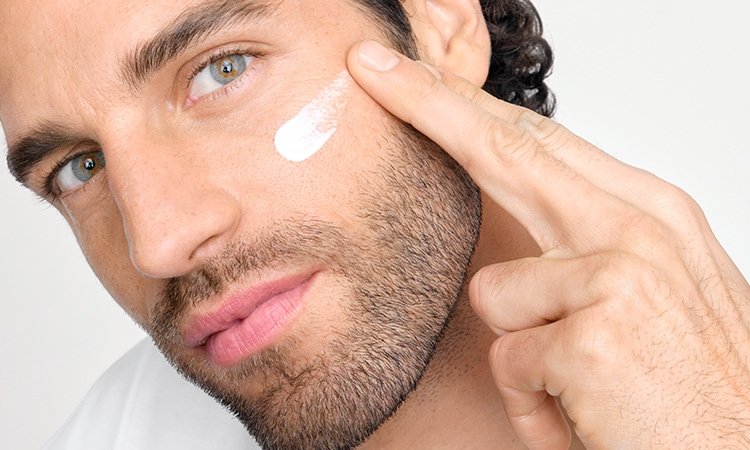 Ein Mann trägt mit zwei Fingern Creme auf der Wangenpartie im Gesicht auf.