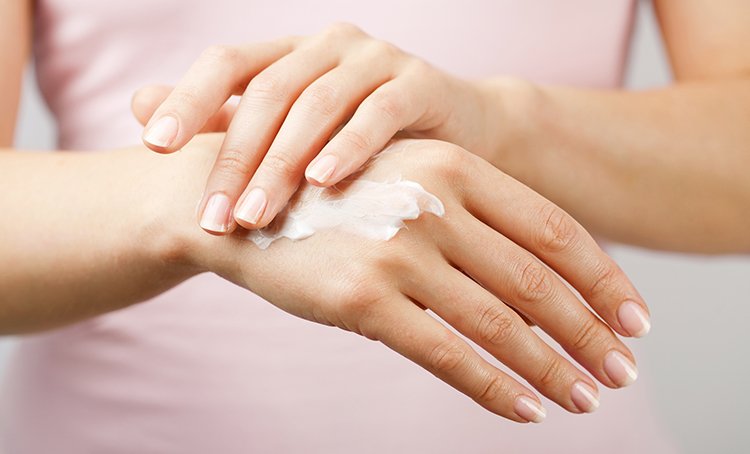 Eine Frau cremt sich ihre Hände mit einer Creme gegen trockene Hände ein