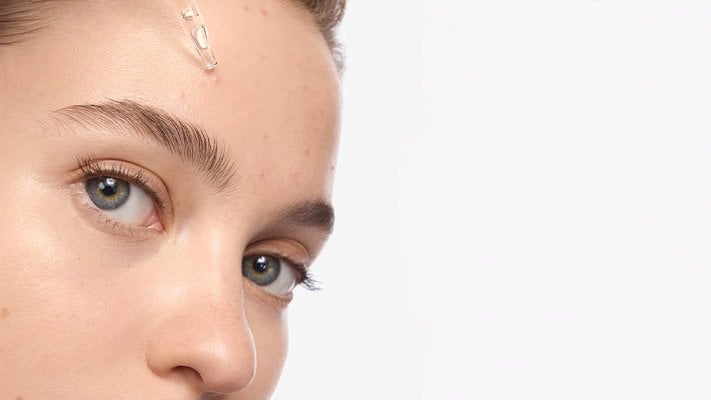 Nahaufnahme eines Gesichts, auf dem aus einer Pipette Serum auf die Stirn aufgetragen wird