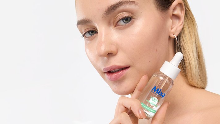 Blonde Frau hält das Mixa Serum mit Salizylsäure neben ihr Gesicht