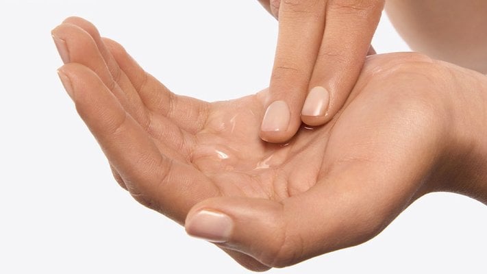 Serum in einer Handfläche wird von Zeige- und Mittelfinger der anderen Hand verteilt