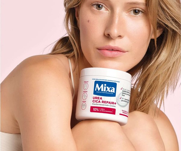 Frau sitzt und hat die Urea Cica Repair+ Hauterneuernde Creme zwischen Knie und Kinn geklemmt